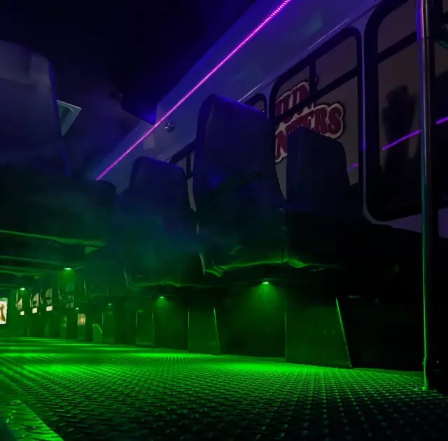 A dark bus interior with neon green and purple lighting illuminating the seats and floor.