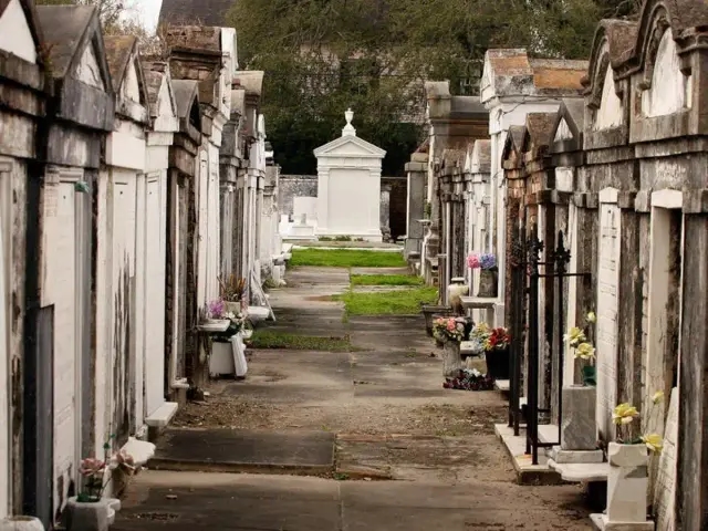 Rows of above-ground tombs in a historic cemetery, lined with flowers and weathered stone pathways.