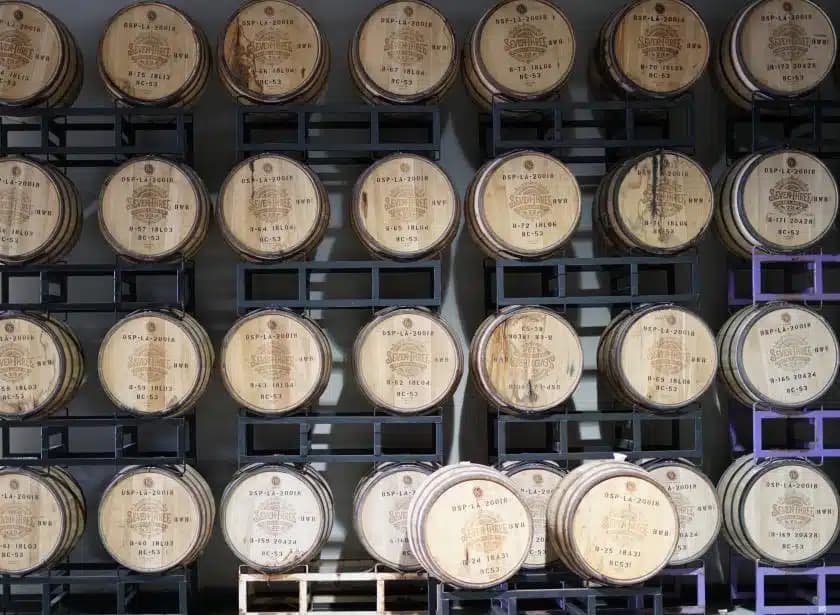 Rows of stacked wooden barrels labeled with distillery markings, arranged on metal racks in a storage facility.