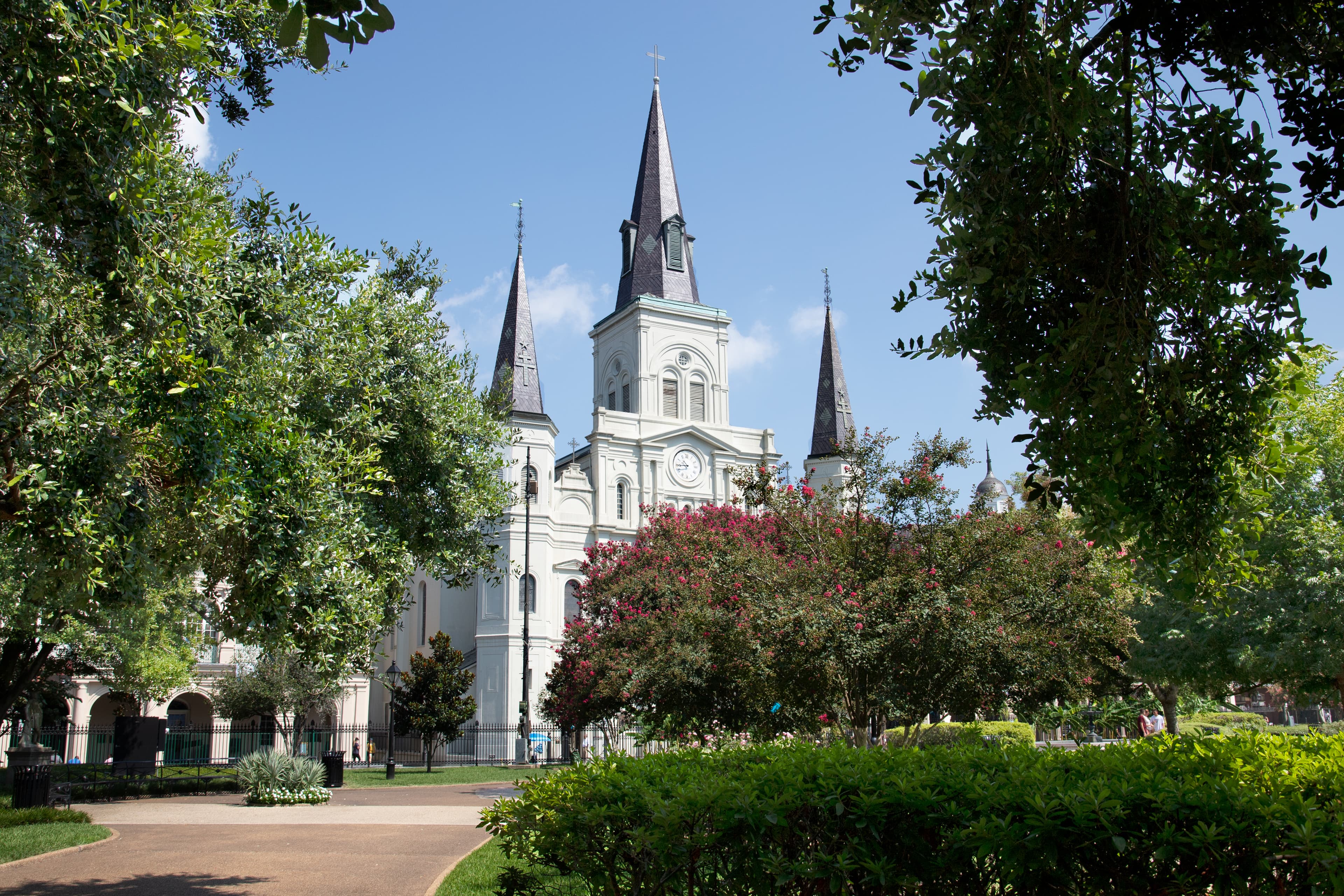 St. Louis Cathedral framed by trees and gardens in Jackson Square, New Orleans, under a clear blue sky.