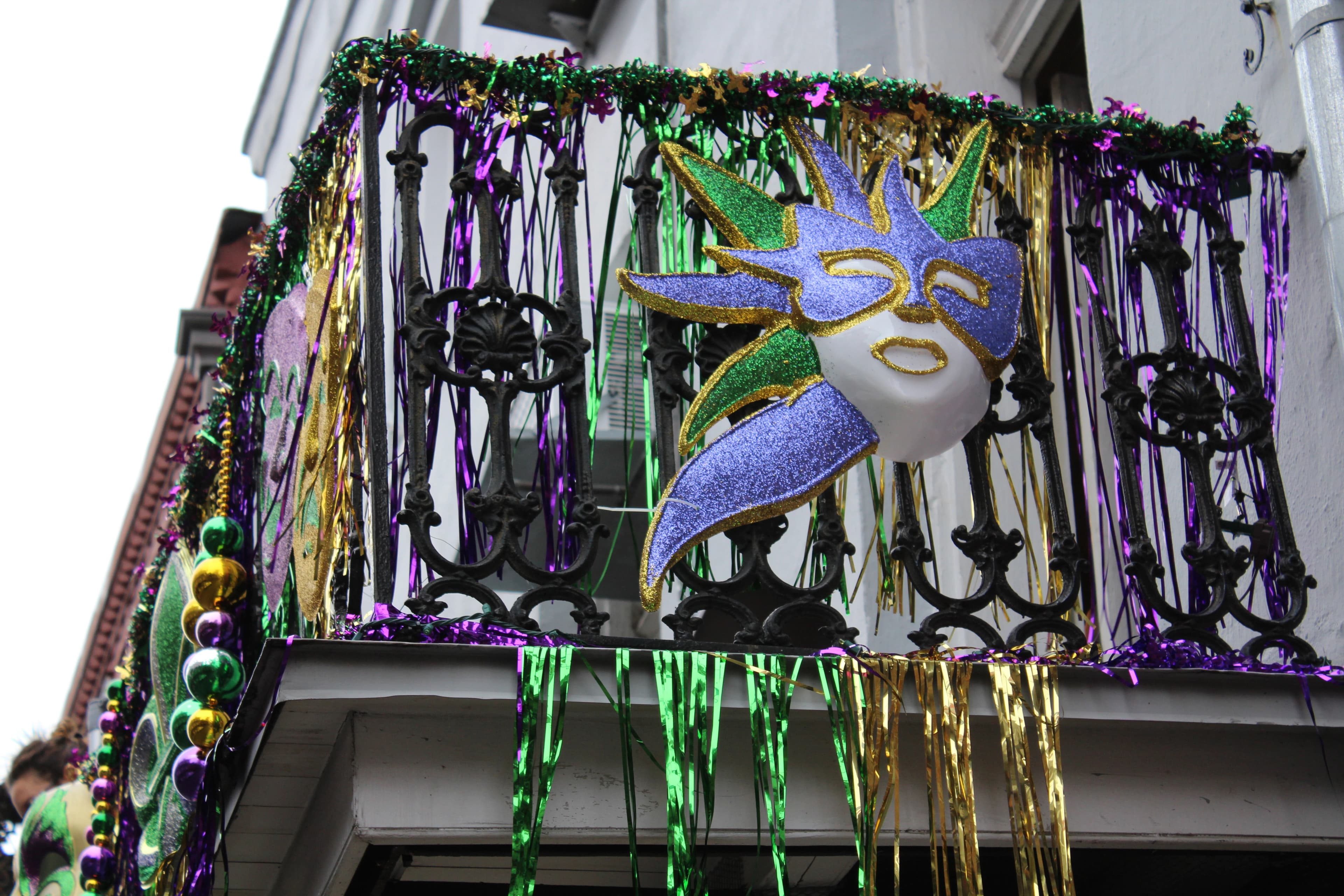 Decorated balcony with Mardi Gras mask, purple, green, and gold garlands, and beads in New Orleans.