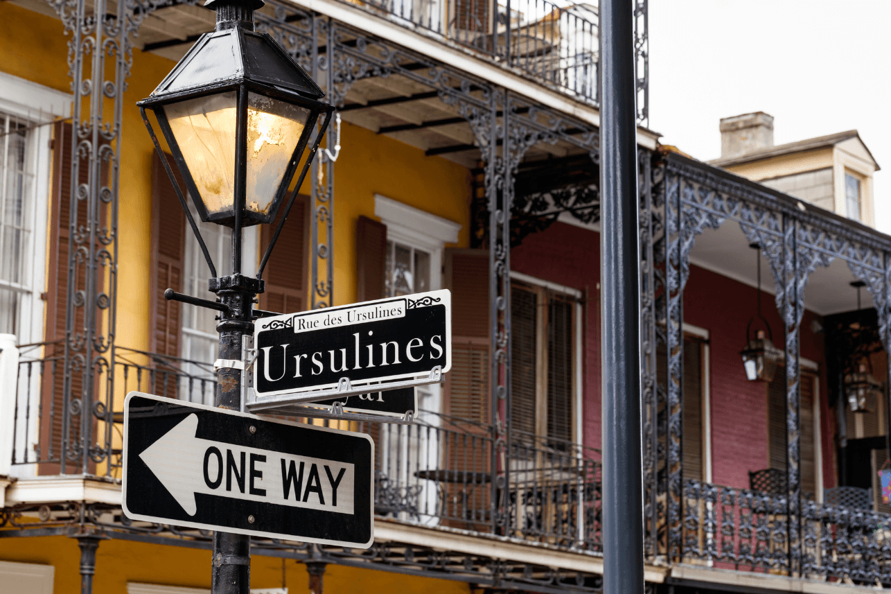 An old fashinoed street sign in new orleans showcasing Ursulines Road with blurred buildings in the background