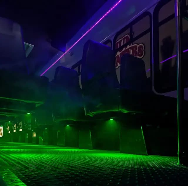 A dark bus interior with neon green and purple lighting illuminating the seats and floor.