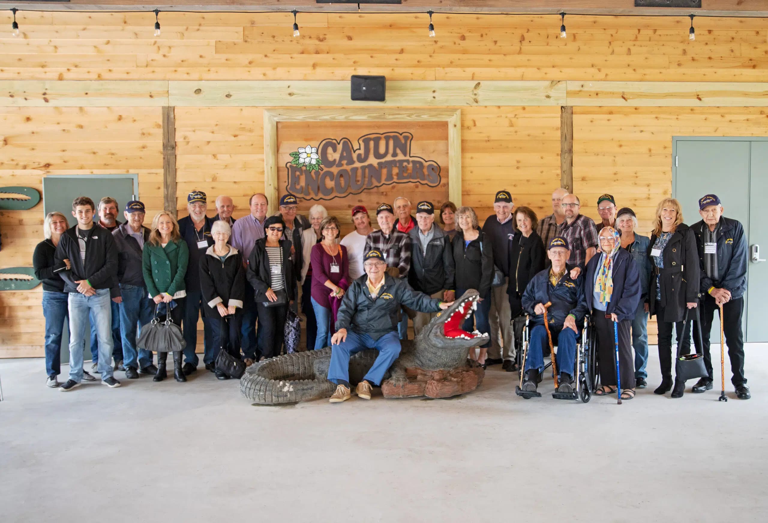 Group of visitors posing in front of the Cajun Encounters sign with a decorative alligator sculpture.