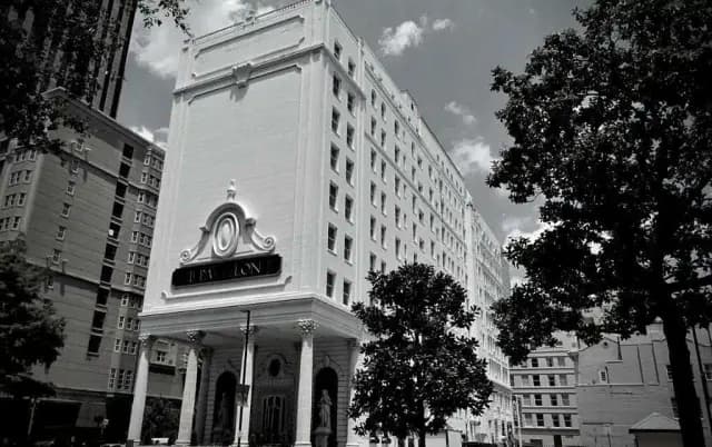 A white, historic hotel building framed by trees, photographed in black and white.