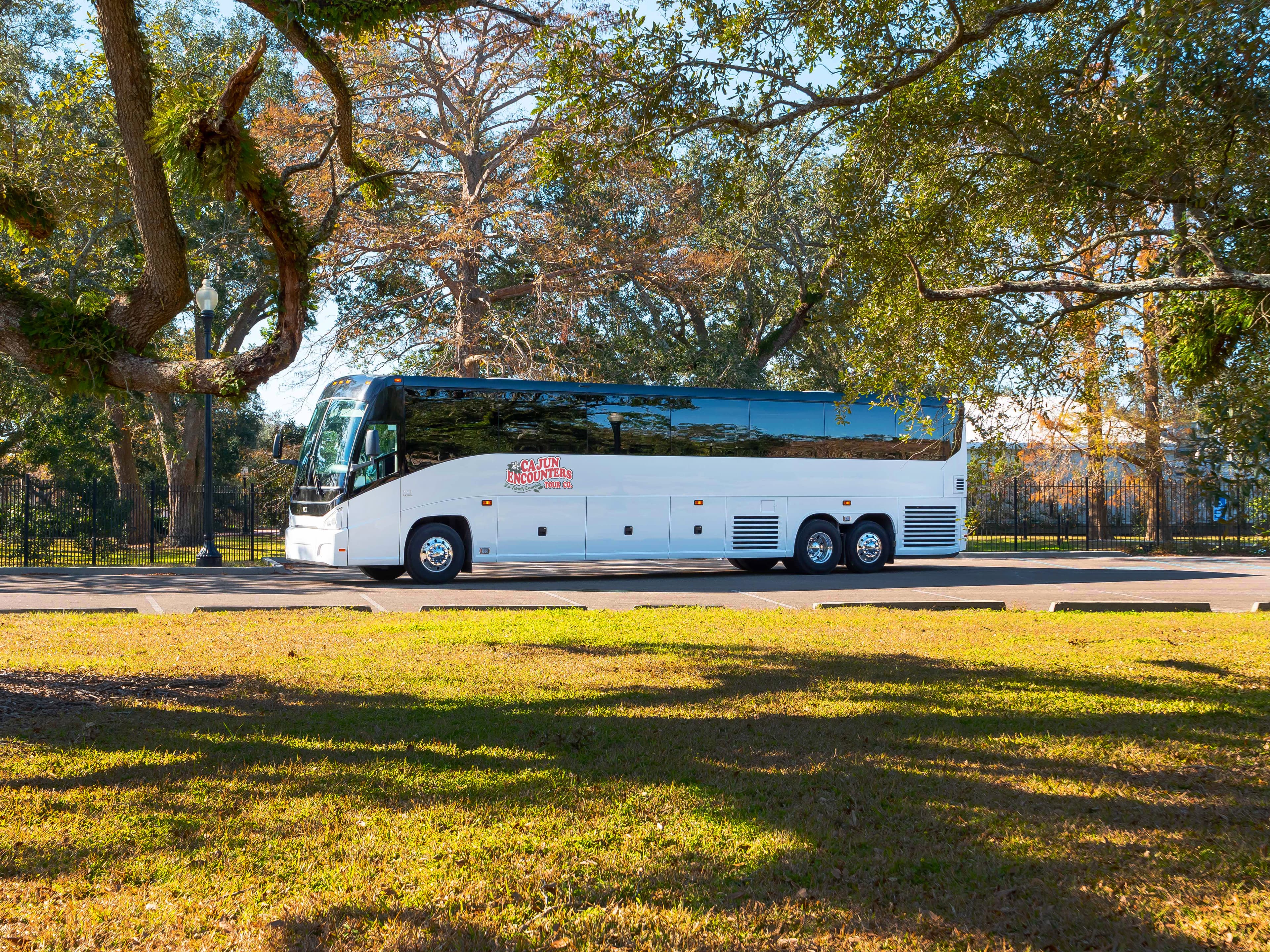 White MCI tour bus labeled 'Cajun Encounters' parked near trees on a sunny day.