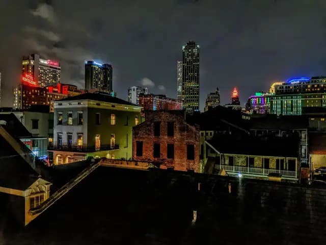 A cityscape of New Orleans at night, showcasing lit-up skyscrapers and colorful building lights.